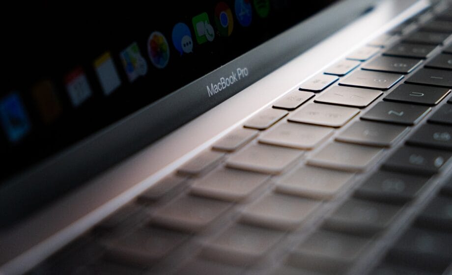 Close-up of a MacBook Pro keyboard with the screen partially visible showing app icons at the top.