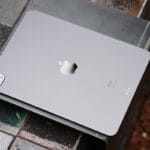 A silver Apple iPad is placed face down on a tiled surface, showing its rear camera and Apple logo.