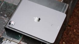 A silver Apple iPad is placed face down on a tiled surface, showing its rear camera and Apple logo.