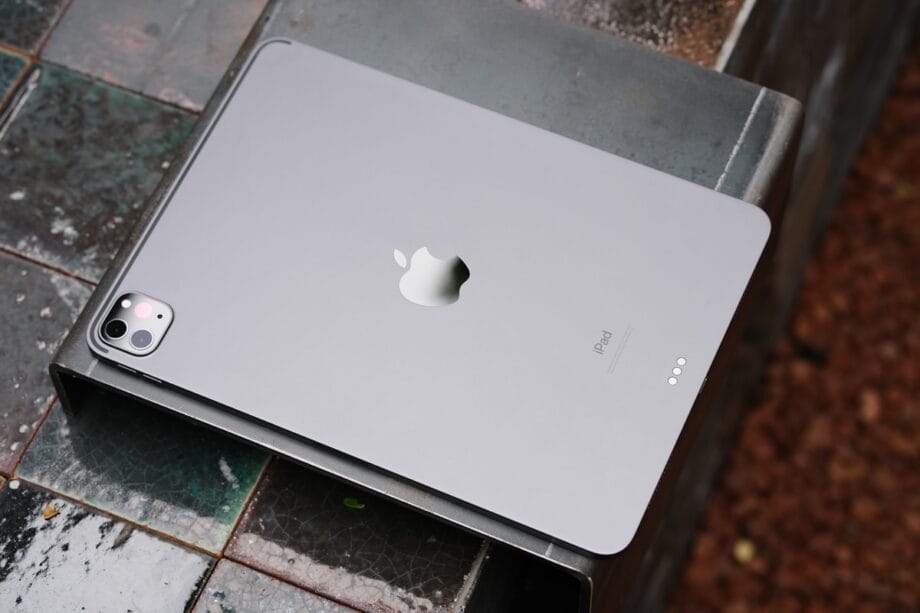 A silver Apple iPad is placed face down on a tiled surface, showing its rear camera and Apple logo.
