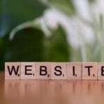 Wooden tiles on a table spell out WEBSITE with a green and white blurred background.