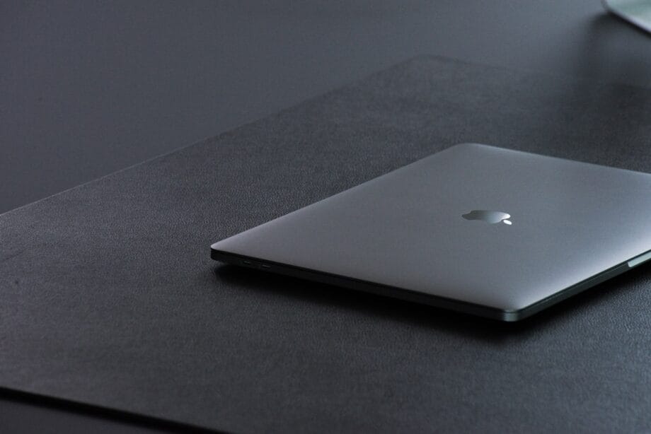 Closed silver MacBook on a black desk mat, with soft light and a minimalist workspace setting.