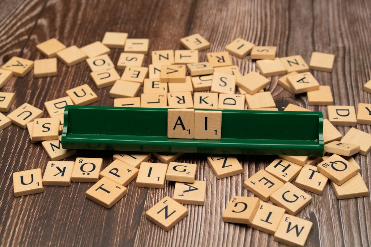 Scrabble tiles spell AI on a green tile rack, surrounded by scattered tiles on a wooden surface.