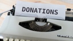 A sheet of paper with the word DONATIONS is inserted into a white typewriter on a wooden surface.