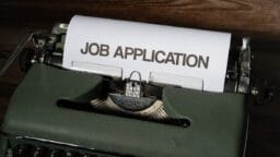 A close-up of a typewriter with a sheet of paper displaying the words JOB APPLICATION in bold uppercase letters.