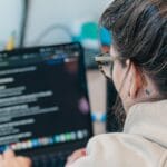 Person with glasses working on a laptop, viewing a dark-themed screen with text and checklists.