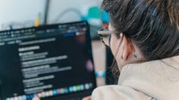 Person with glasses working on a laptop, viewing a dark-themed screen with text and checklists.