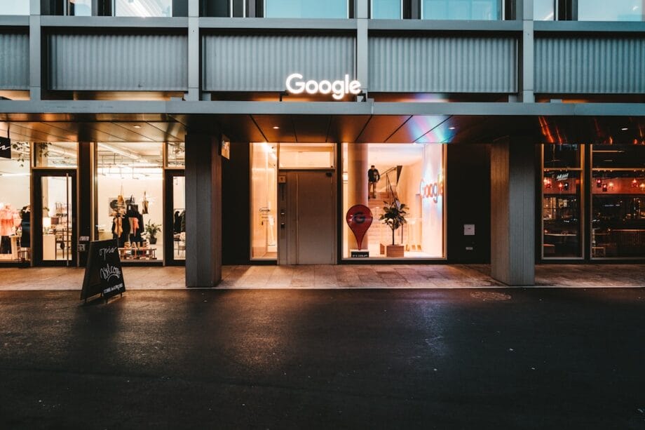 Exterior view of a Google office entrance with illuminated signage and glass doors, taken at street level in the evening.