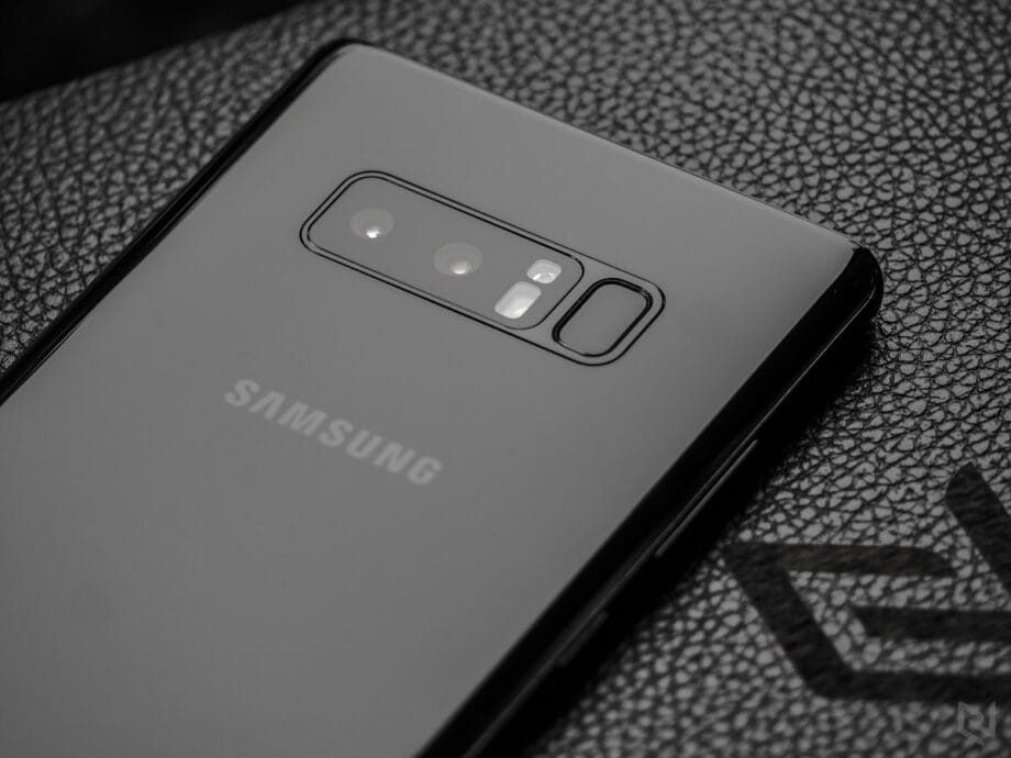 Close-up of the back of a black Samsung smartphone showing dual cameras and fingerprint sensor on a textured surface.