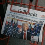 A Le Monde newspaper headline announces Donald Trump’s election win with his photo, displayed in a red wire rack.