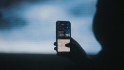 A person holds a smartphone, live streaming video and typing in a chat with emojis visible on the screen.