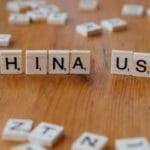 Scrabble tiles on a wooden surface spell out CHINA and USA with other scattered letter tiles in the background.