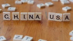 Scrabble tiles on a wooden surface spell out CHINA and USA with other scattered letter tiles in the background.