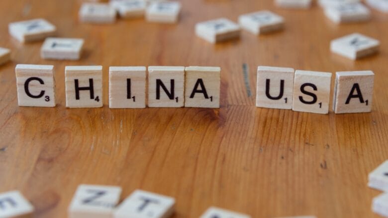 Scrabble tiles on a wooden surface spell out CHINA and USA with other scattered letter tiles in the background.