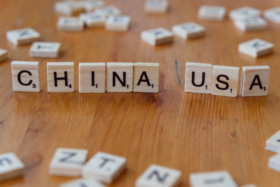 Scrabble tiles on a wooden surface spell out CHINA and USA with other scattered letter tiles in the background.