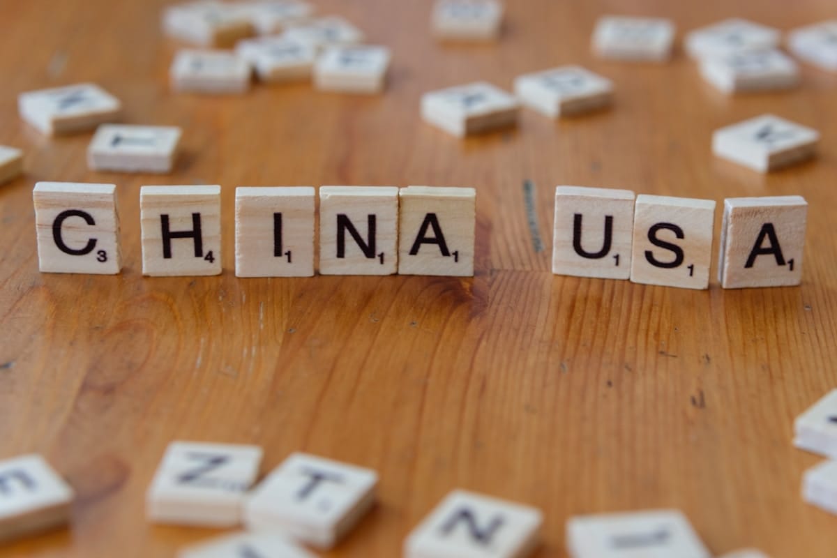 Scrabble tiles on a wooden surface spell out CHINA and USA with other scattered letter tiles in the background.