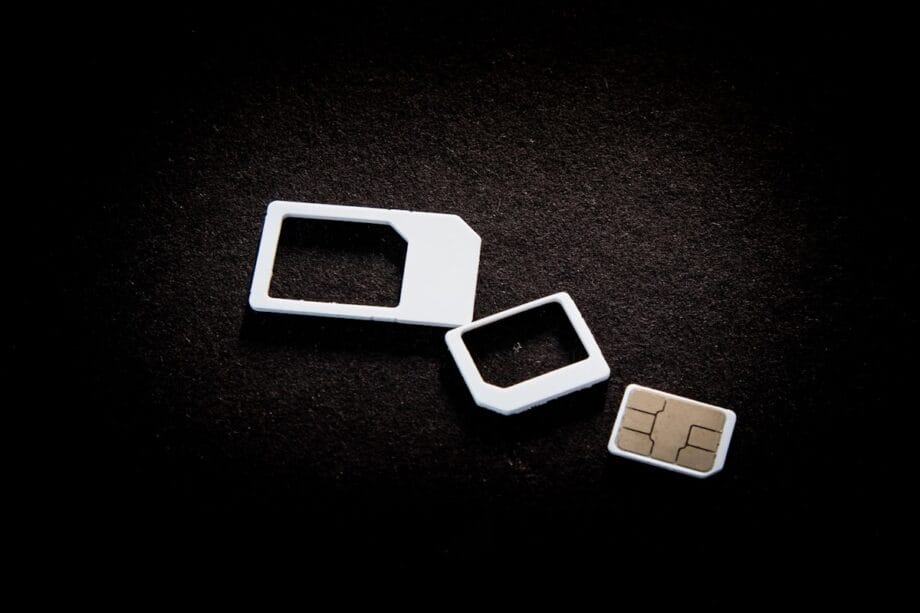 A SIM card with two white plastic adapters is placed on a black surface.