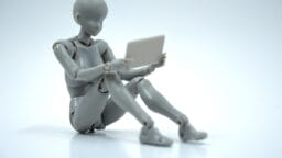 A gray humanoid mannequin sits on the ground holding a tablet against a plain white background.