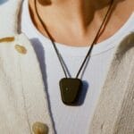 Person wearing a white shirt and cream cardigan with a Fieldy device on a cord around their neck.