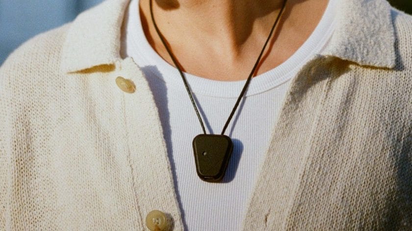 Person wearing a white shirt and cream cardigan with a Fieldy device on a cord around their neck.