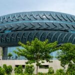 A modern building with an upper structure designed to resemble a large, horizontal tire, surrounded by trees and greenery.