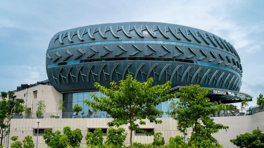 A modern building with an upper structure designed to resemble a large, horizontal tire, surrounded by trees and greenery representing industrial rubber technologies.