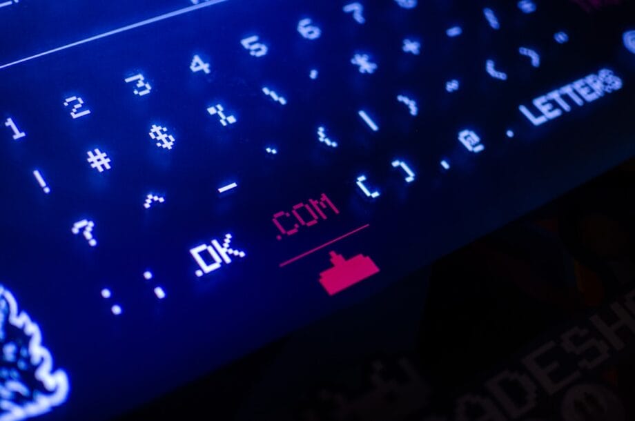 Close-up of a digital keyboard display with the text OK .COM highlighted and a red ship icon below.