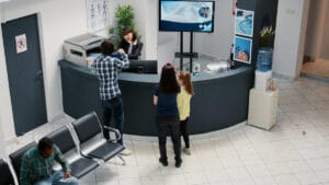 A man checks in at a circular reception desk while a woman and child stand nearby in a medical waiting area.