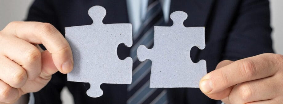 A person in a suit holds two large puzzle pieces close together, as if about to connect them.