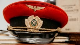 A red and black peaked cap with gold insignia, including wings and crossed hammers, rests on a stack of papers.