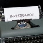 A typewriter with a sheet of paper displaying the word INVESTIGATION in large letters.