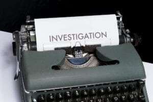 A sheet of paper with the word “INVESTIGATION” is loaded in a vintage typewriter.