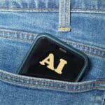 A smartphone with AI on its screen is partially visible in the back pocket of blue denim jeans.