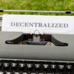 A typewriter with a sheet of paper displaying the word Decentralized set outdoors on grass.