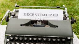 A typewriter with a sheet of paper displaying the word Decentralized set outdoors on grass.