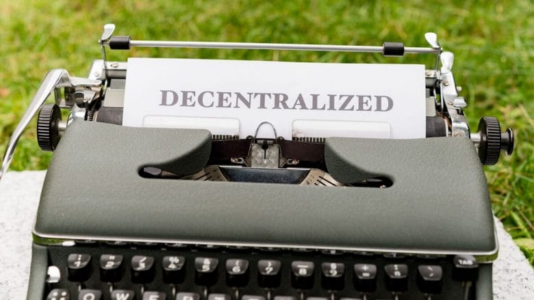 A typewriter with a sheet of paper displaying the word Decentralized set outdoors on grass.