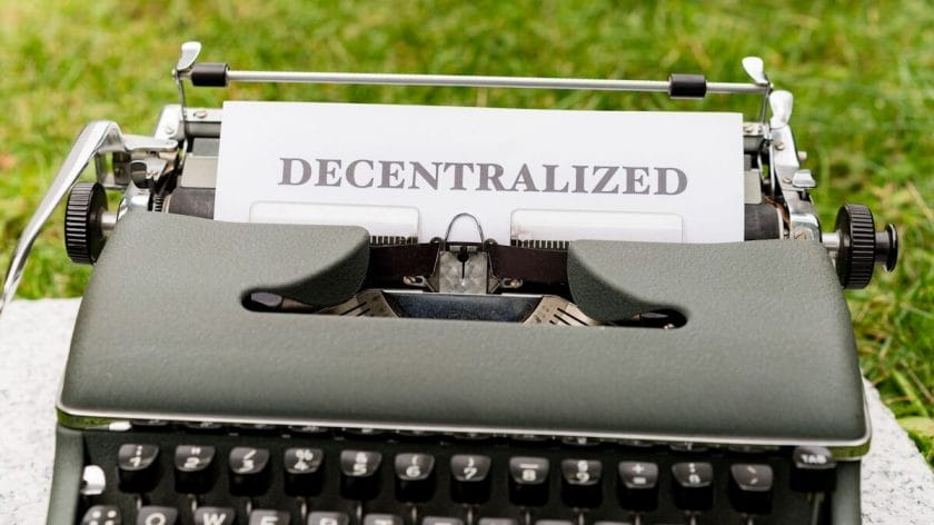 A typewriter with a sheet of paper displaying the word Decentralized set outdoors on grass.