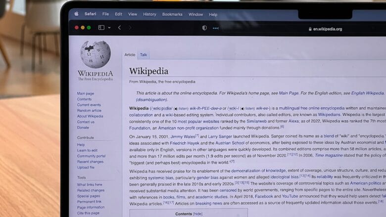 A laptop screen displays the Wikipedia homepage with text and navigation menus visible in a bright indoor setting.