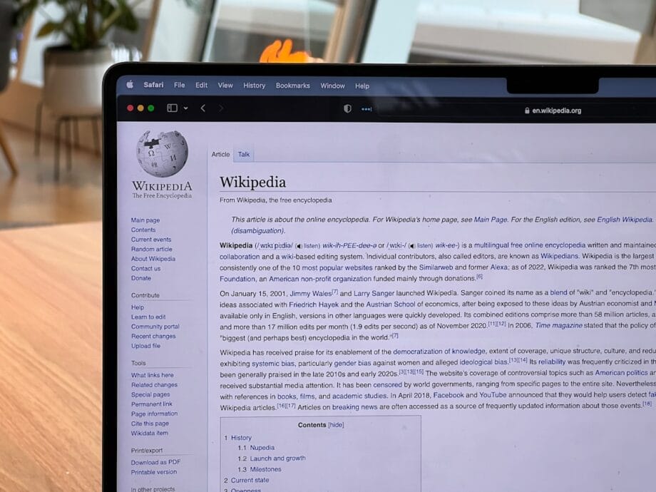 A laptop screen displays the Wikipedia homepage with text and navigation menus visible in a bright indoor setting.