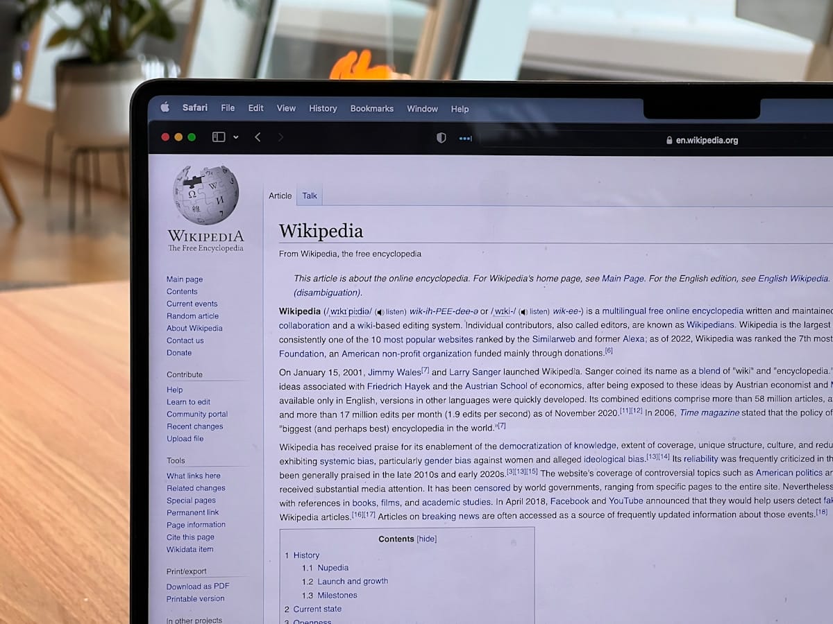 A laptop screen displays the Wikipedia homepage with text and navigation menus visible in a bright indoor setting.