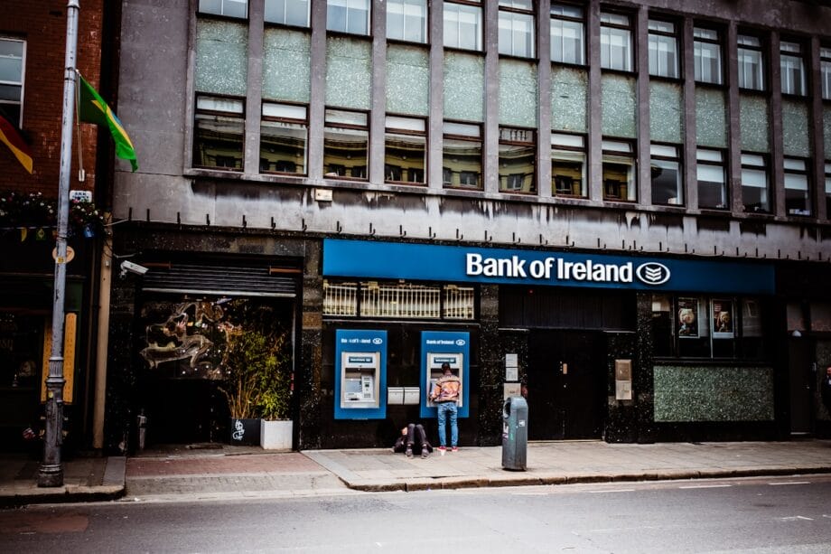 Person using an ATM outside a Bank of Ireland branch on a city street during daytime.