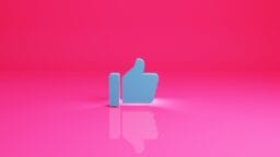 A blue thumbs-up like icon stands upright on a reflective pink surface with a pink background.