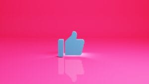 A blue thumbs-up like icon stands upright on a reflective pink surface with a pink background.