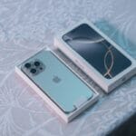 A silver iPhone partially out of its box sits beside the box lid on a patterned tablecloth.