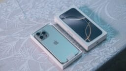 A silver iPhone partially out of its box sits beside the box lid on a patterned tablecloth.