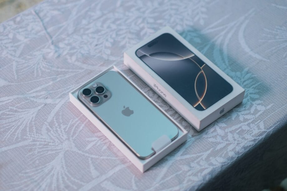 A silver iPhone partially out of its box sits beside the box lid on a patterned tablecloth.