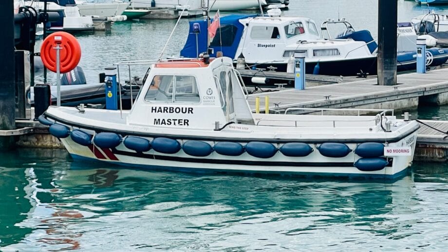 Small white Harbour Master boat docked at a marina, surrounded by water and several other boats in the background.