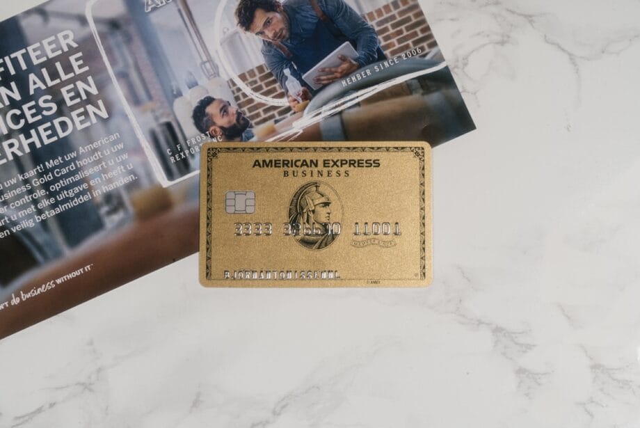 A gold American Express Business credit card lies on a marble surface next to a brochure with text in Dutch.