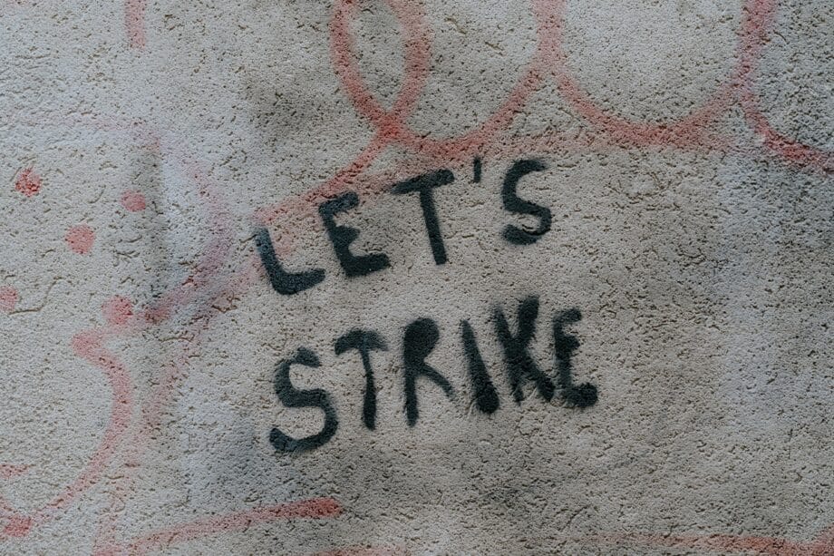 The words LETS STRIKE are spray-painted in black on a rough, light-colored wall with faint red markings in the background.