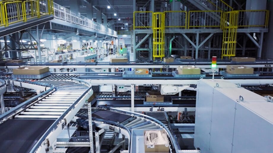 Automated conveyor belts transport cardboard boxes through a large industrial warehouse or distribution center.